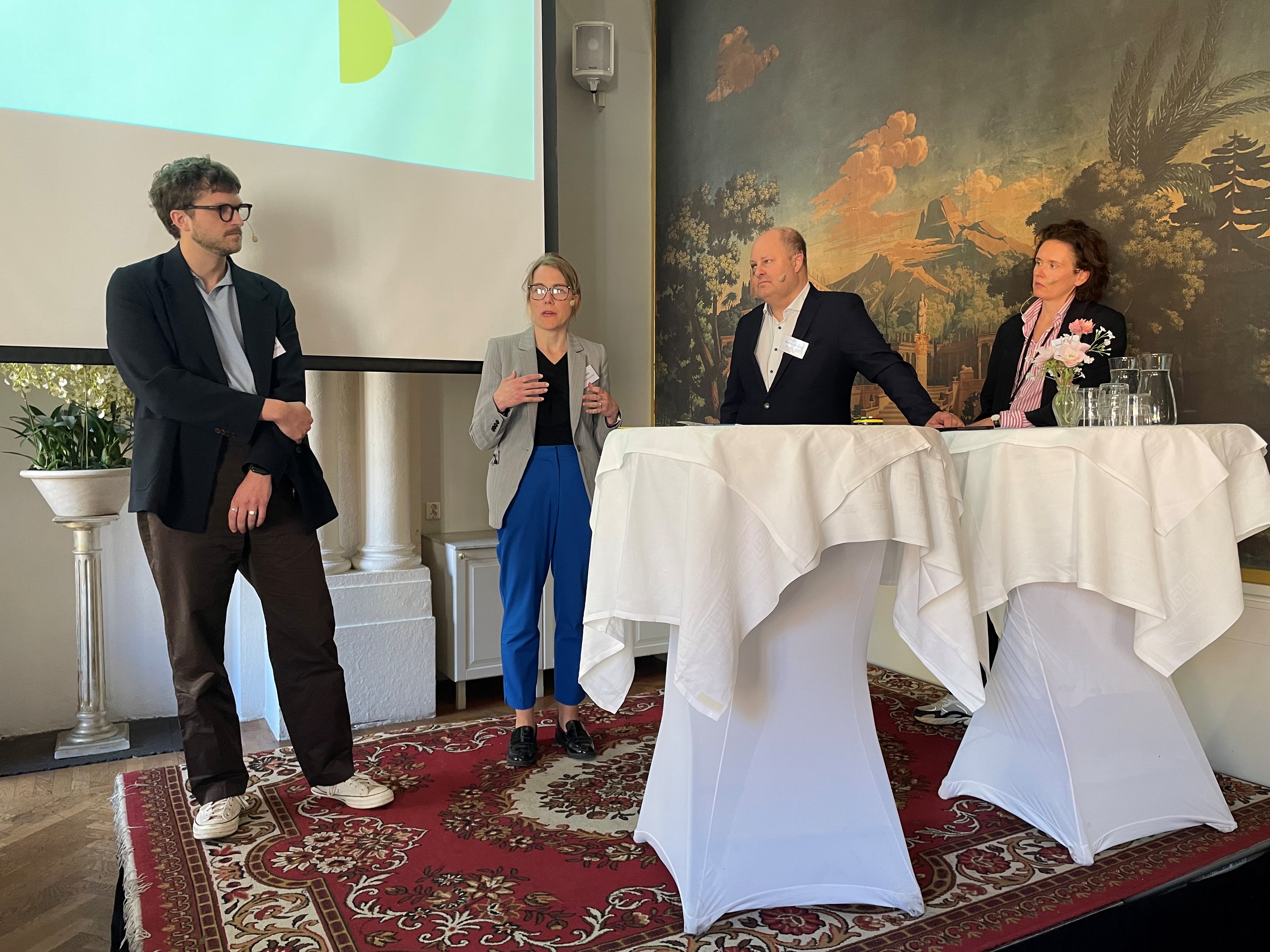 Fyra personer i panel på konferens står på en scen.